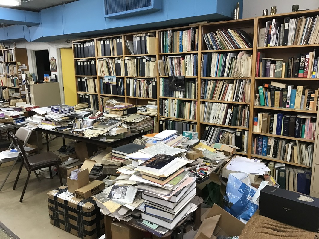 Bookshelves and tables filled with books, binders, and research papers.