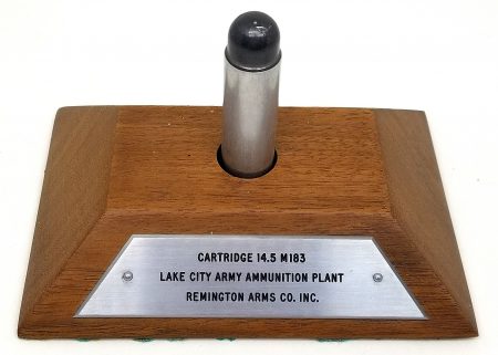 Lot 65 - Lake City Army Ammunition plant display of a 14.5mm M183 (dummy, no primer) cartridge on a wood base. Aluminum case is headstamped “L C 7 0” and the lead projectile slides out easily for inspection. Remington Arms Co. Inc. contractor. Project failed, so this is a rare display and headstamp. Ex-Woodin collection. $250-325