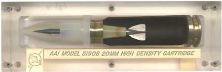 Lot 96 - AAI 20mm Model 51908 “High Density Cartridge.” with a steel flechette projectile 4.1 inches long in a sectioned case. The round is displayed in a clear Lucite box held together with screws. Ex-Woodin collection. $325-375